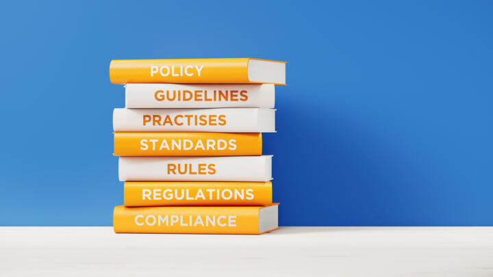 A stack of books showing policy, guidelines, practice, rules, regulation and compliance.