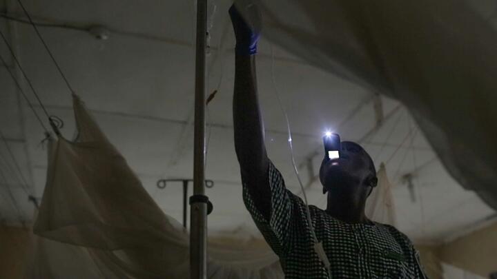 A nurse uses his cell phone for light at a hospital in Liberia that has no electricity